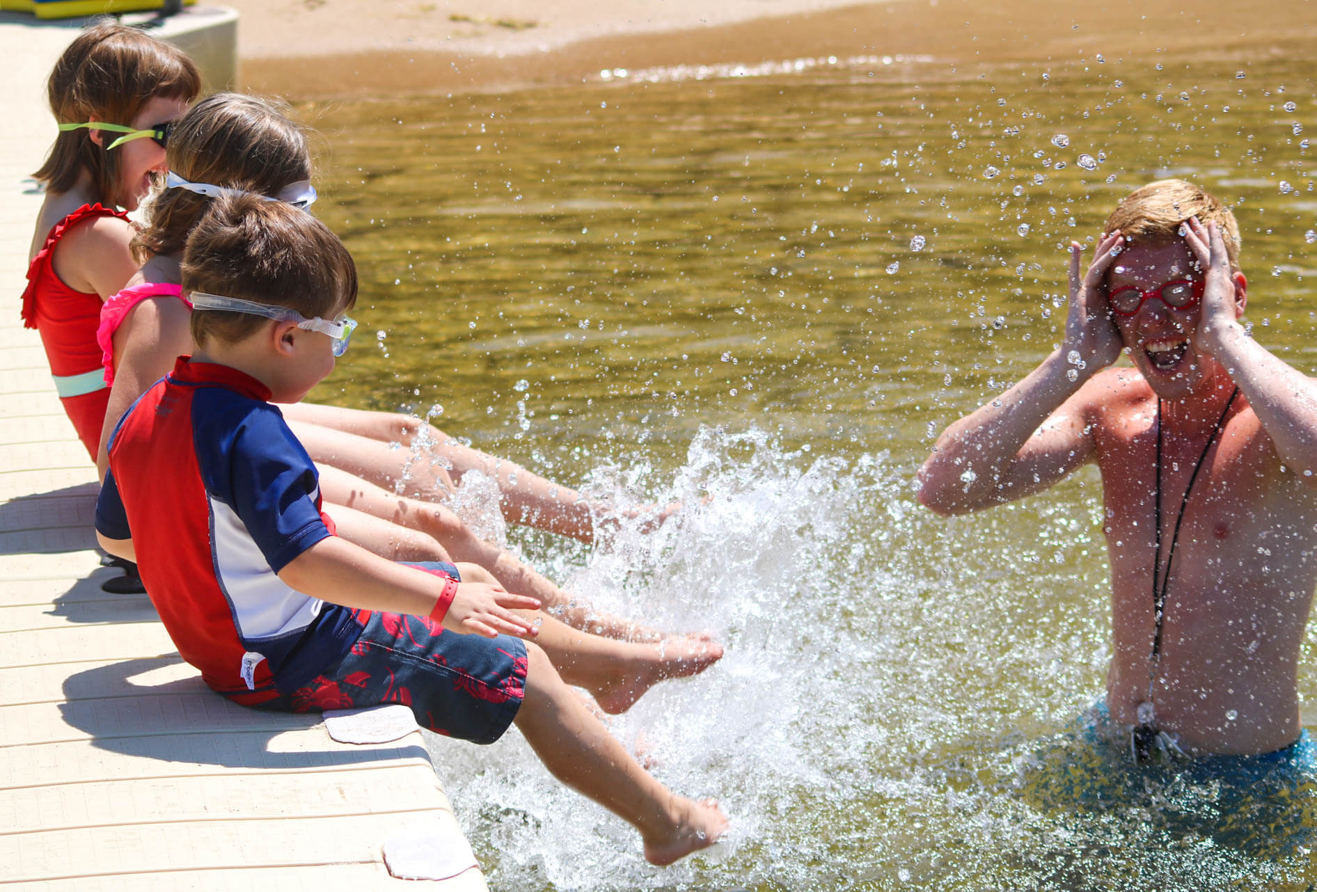 Young campers sit on dock and splash counselor